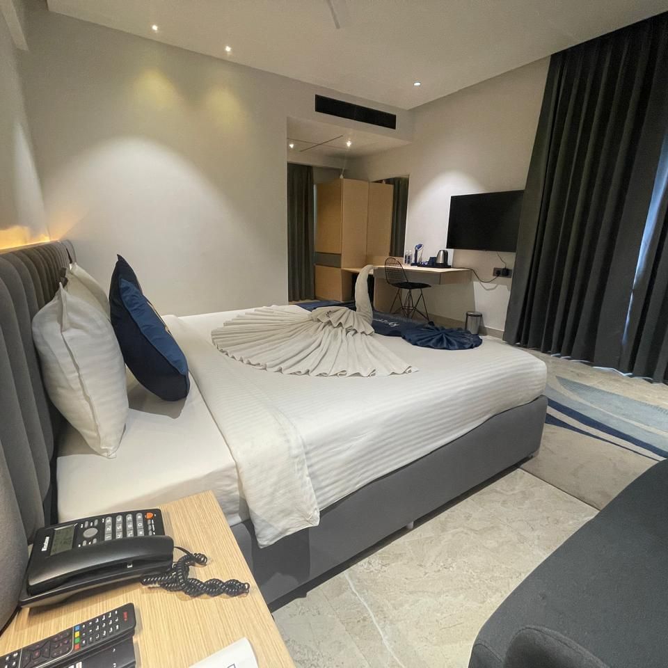 Bedroom at Hotel Kyzen HiTech City with a king bed, side table and curtained windows.